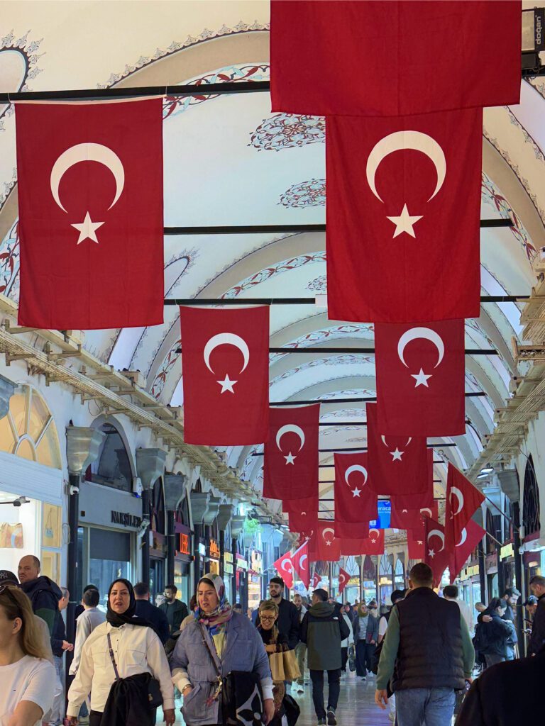 Turkish flags hanging above busy Grand Bazaar Istanbul aisle, lively itinerary highlight
